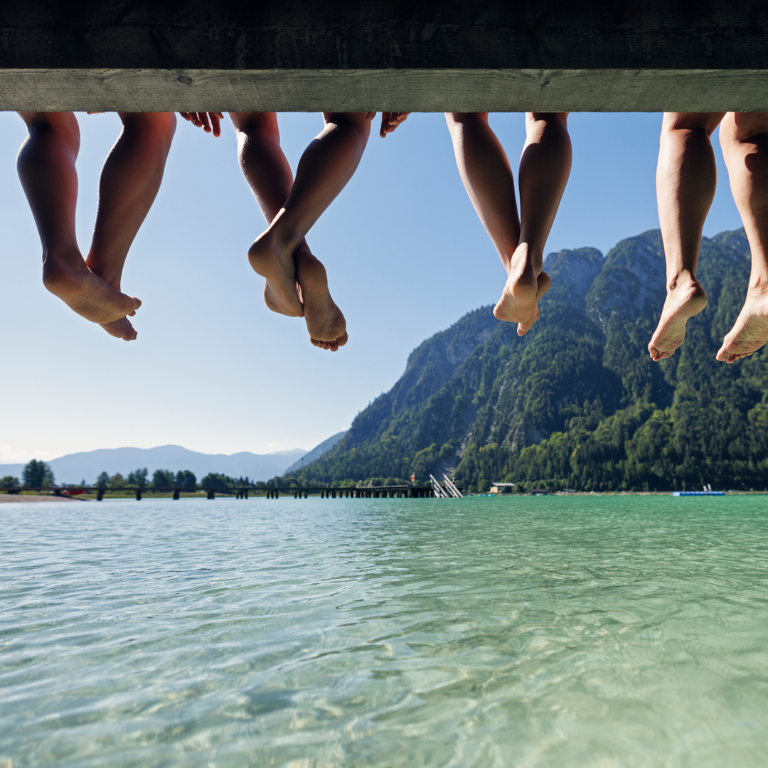 Pieds de plusieurs personnes assises sur un ponton au-dessus d'un lac de montagne : atelier communication d'une demi-journée