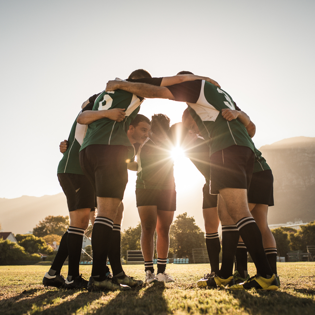 Joueurs en cercle, bras sur les épaules, à contre-jour : cohésion d'équipe et storytelling d'entreprise