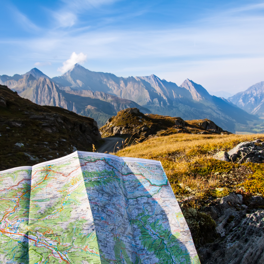 Carte de randonnée dépliée face à des sommets alpins : trouver son itinéraire en communication
